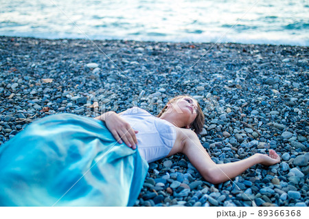 Beautiful long haired woman dressed a mermaid sitting on the sand beach background 89366368