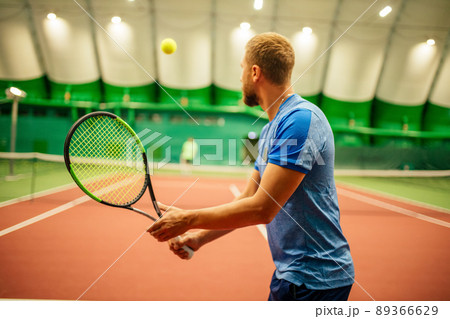 Instructor or coach teaching how to play tennis on a court indoor Instructor or coach teaching how to play tennis on a court indoor 89366629