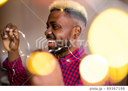 african man making preparations for Christmas party and decorating home with glowing garland 89367198