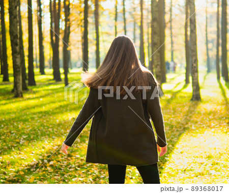 Girl with long dark hair is spinning in Park in sunlight. Woman stands with her back, facing sun, looking forward 89368017