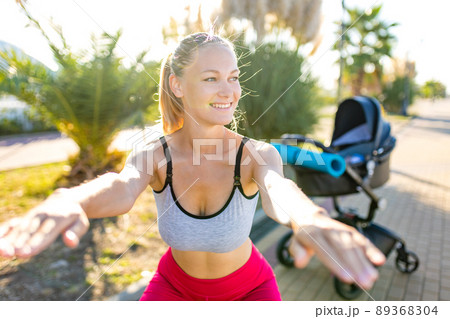 blonde yound mom working out outdoors warming up with yoga mat in tropical beach 89368304