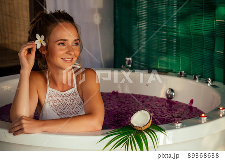 Woman relaxing in bath with tropical flowers outdoor at luxury hotel. 89368638