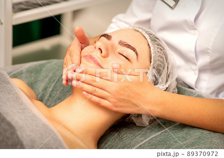 Beautiful caucasian young woman receiving a facial massage with closed eyes in spa salon, close up. Relaxing treatment concept 89370972
