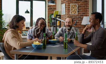 Happy group of people enjoying board strategy with cards and dice, having fun with modern competitive game at home. Men and women playing party games activity for entertainment. 89372453