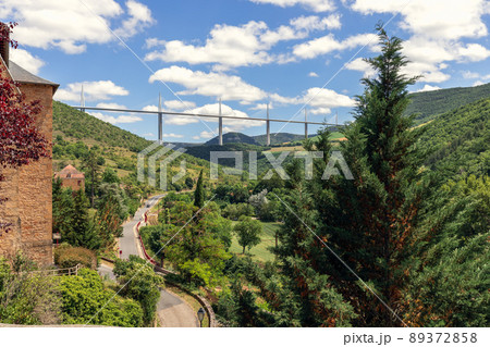 Old valley road D41 enters Peyre village and Millau Viaduct on background. Aveyron, Occitania 89372858