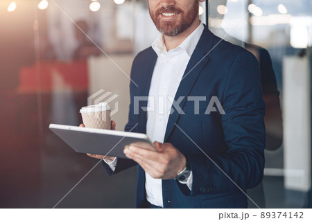 Close up of smiling businessman with take away coffee cup working on laptop at modern office 89374142