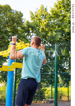 A man is exercising on the street. Opening gym outdoors on the sports ground in a green park. A man is exercising on the street. Opening gym outdoors on the sports ground in a green park. 89374781
