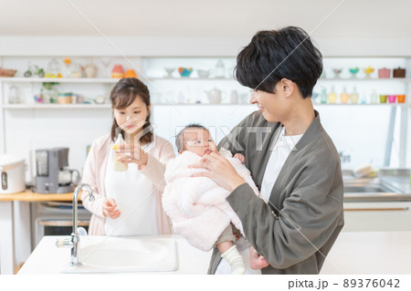 赤ちゃんを抱っこする新米パパとミルクを作るママ 赤ちゃんを抱っこする新米パパとミルクを作るママ 89376042