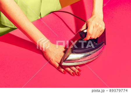 Colorful bright image of female hand ironing her hand with retro iron isolated over pink yellow background 89379774