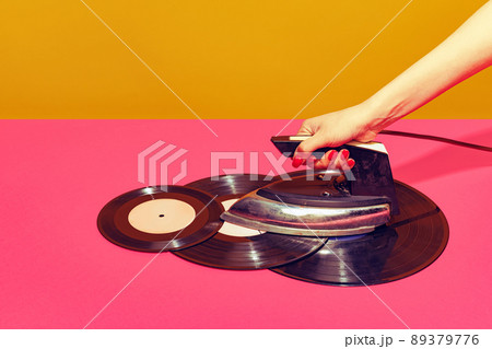 Colorful bright image of woman using retro iron and ironing vintage vinyl records isolated over pink background. Creativity 89379776