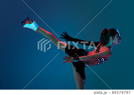 Dynamic portrait of young girl, female figure skater in black stage dress skating isolated on blue background in neon light. Concept of sport, beauty, active lifestyle. Dynamic portrait of young girl, female figure skater in black stage dress skating isolated on blue background in neon light. Concept of sport, beauty, active lifestyle. 89379797