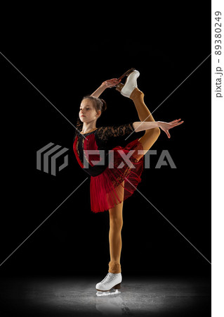 Studio shot of little female figure skater in beautiful stage attire skating isolated on black background in spotlight. Concept of movement, sport, beauty. Studio shot of little female figure skater in beautiful stage attire skating isolated on black background in spotlight. Concept of movement, sport, beauty. 89380249