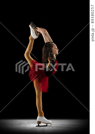 Studio shot of little female figure skater in beautiful stage attire skating isolated on black background in spotlight. Concept of movement, sport, beauty. Studio shot of little female figure skater in beautiful stage attire skating isolated on black background in spotlight. Concept of movement, sport, beauty. 89380257