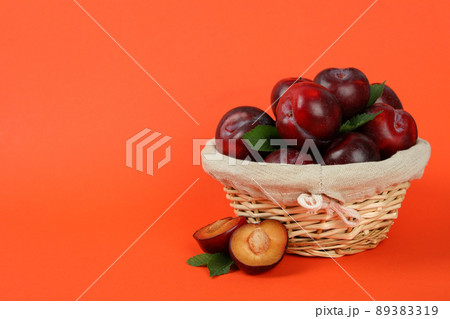 Wicker bowl with plums on an orange background 89383319