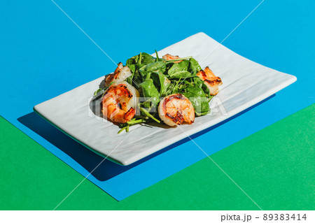 Salad with shrimps and arugula on white dish on colored background Salad with shrimps and arugula on white dish on colored background 89383414