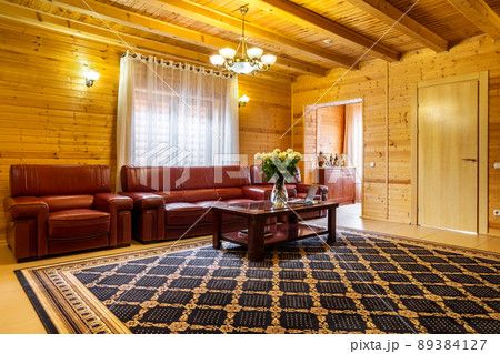 Cozy living room in country house with natural wood trim, leather sofa set and coffee table Cozy living room in country house with natural wood trim, leather sofa set and coffee table 89384127