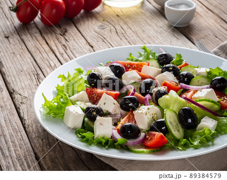 Greek salad on white plate on old rustic wooden table, side view Greek salad on white plate on old rustic wooden table, side view 89384579