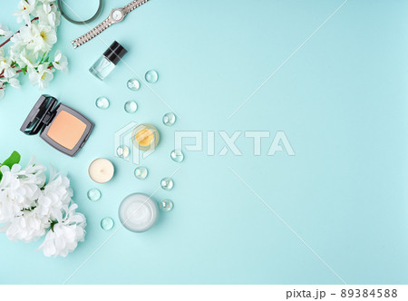 Flat lay woman accessories with cosmetic, facial cream, bag, flowers on pastel blue table. 89384588