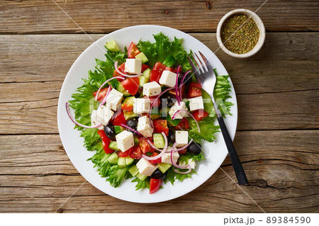 Greek salad on white plate on old rustic wooden table, top view Greek salad on white plate on old rustic wooden table, top view 89384590