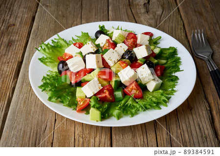 Greek salad on white plate on old rustic wooden table, side view Greek salad on white plate on old rustic wooden table, side view 89384591
