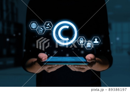 The concept of copyright and intellectual property as a projection of a hologram over a tablet in the hands of a person. The concept of copyright and intellectual property as a projection of a hologram over a tablet in the hands of a person. 89386197