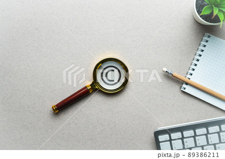 The concept of copyright and intellectual property. Magnifier with icon on the table. 89386211