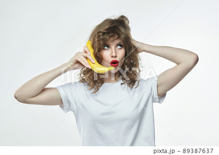 attractive girl holds a banana in her hands and pretends to call through it attractive girl holds a banana in her hands and pretends to call through it 89387637