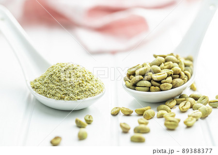 Ground green coffee and unroasted coffee beans on white table. Ground green coffee and unroasted coffee beans on white table. 89388377