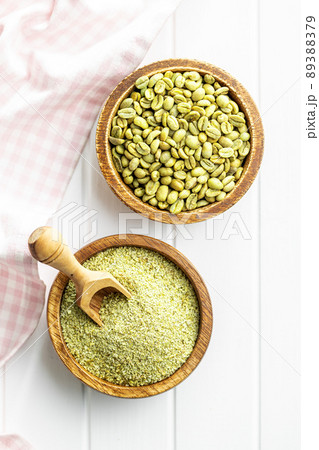 Ground green coffee and unroasted coffee beans on white table. Ground green coffee and unroasted coffee beans on white table. 89388379