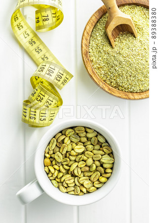 Ground green coffee and unroasted coffee beans on white table. 89388380