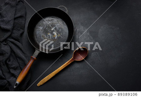 Empty round cast iron frying pan with wooden handle on black table, top view Empty round cast iron frying pan with wooden handle on black table, top view 89389106