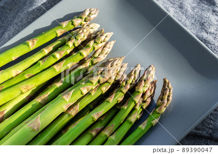 Close-up detail bunch of fresh raw green asparagus plant harvested at season on blue cerami plate kitchen background. Healthy vegeterain gourmet vegetable food. Health vegan diet nutrition concept Close-up detail bunch of fresh raw green asparagus plant harvested at season on blue cerami plate kitchen background. Healthy vegeterain gourmet vegetable food. Health vegan diet nutrition concept 89390047
