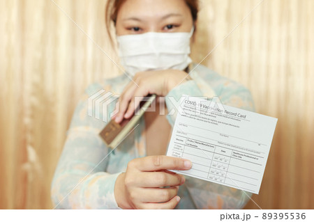 Woman in travel clothes wearing a medical mask showing covid-19 vaccination record card and passport. Travel concept with vaccination.selective focus. Woman in travel clothes wearing a medical mask showing covid-19 vaccination record card and passport. Travel concept with vaccination.selective focus. 89395536