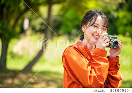 屋外でレトロなフィルムカメラで趣味の写真を撮る若い女性 89396919