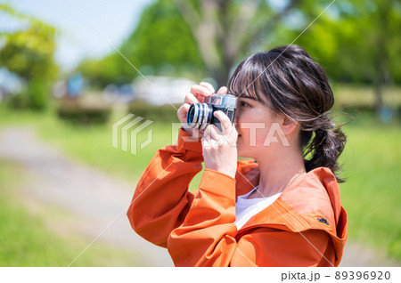 屋外でレトロなフィルムカメラで趣味の写真を撮る若い女性 89396920