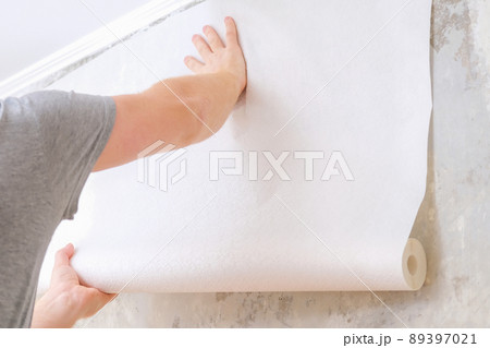 A man rolls out a roll of white wallpaper on the 89397021