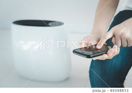 Woman control a modern air purifier through the application on a smartphone, a smartphone screen isolated in white color. Modern and smart home connectivity technology concept. Woman control a modern air purifier through the application on a smartphone, a smartphone screen isolated in white color. Modern and smart home connectivity technology concept. 89398653