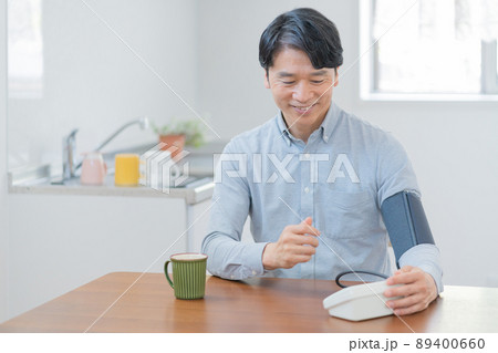 リビングで血圧計で血圧を測る笑顔の中年男性 リビングで血圧計で血圧を測る笑顔の中年男性 89400660