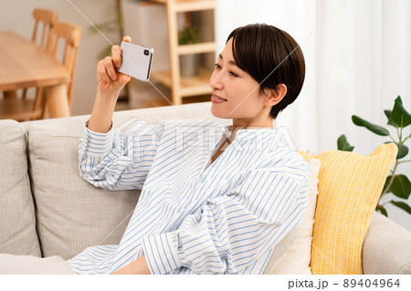 ソファーに座りながらスマートフォンを使う若い女性 ソファーに座りながらスマートフォンを使う若い女性 89404964
