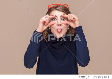 Crazy woman looking at camera and tongue out. Studio shot, light brown background 89405484