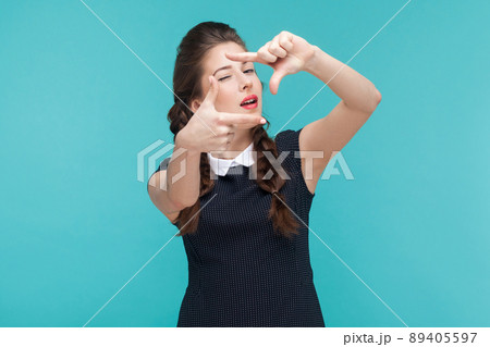 Well dressed young woman showing frame sign and wink. Indoor, studio shot on blue background 89405597