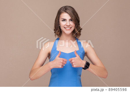 Cute business woman showing like sign and toothy smile. Studio shot, light brown background 89405598