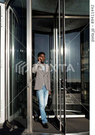 End of working day. African American manager going through glass revolving door and talking on smartphone 89411442