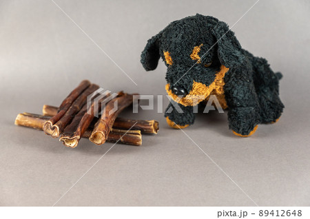 Pet treats and a children's toy opposite the gray background. Natural dried treats and a black stuffed dog. Bully sticks. Pet supplies. Pet treats and a children's toy opposite the gray background. Natural dried treats and a black stuffed dog. Bully sticks. Pet supplies. 89412648
