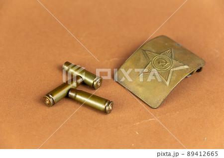 Soviet belt buckle and empty shell casings against brown background. Attribute of the Red Army soldier's military clothing. Three automatic rifle casings. 89412665