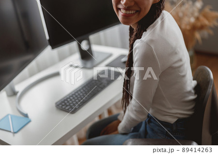 Close up of unrecognizable young positive woman indoor at table with computer monitors Close up of unrecognizable young positive woman indoor at table with computer monitors 89414263