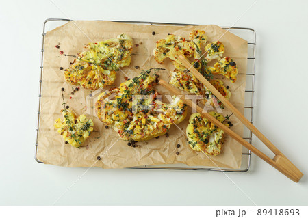 Baking rack with baked cauliflower and wooden tongs on white background 89418693