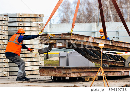 Slinger in helmet and vest controls unloading of metal structures on construction site. White 89419738