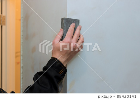 Worker sanding the drywall mud using sand trowel during renovation the house Worker sanding the drywall mud using sand trowel during renovation the house 89420141