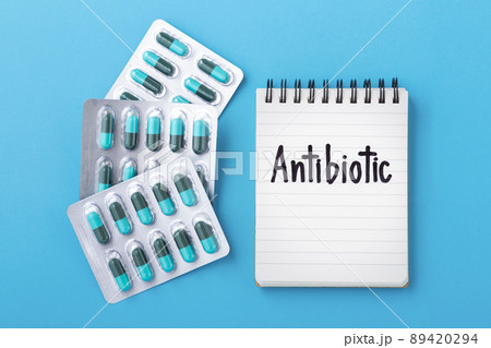 Antibiotic capsule pills in pack with notebook on blue background, top view 89420294